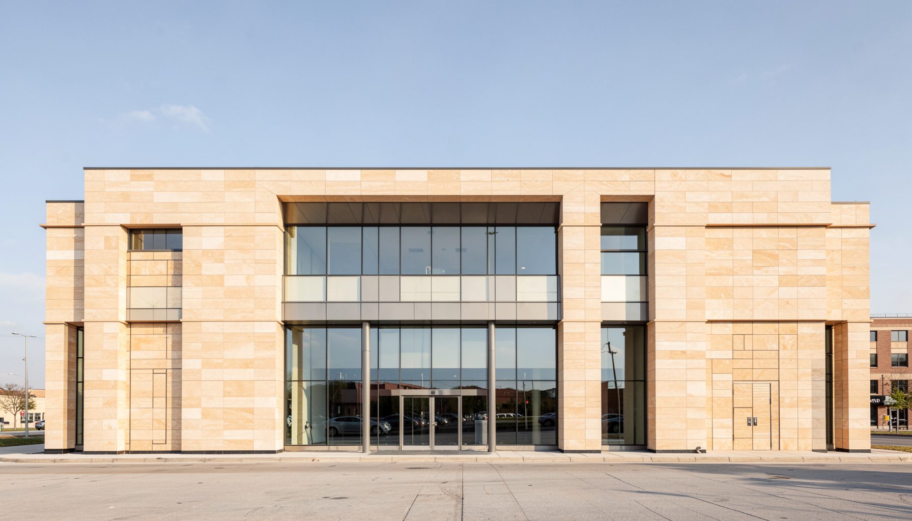 A clean, symmetrical architectural photograph of a modern transportation agency building facade with strong horizontal lines, warm beige stone, and reflective glass under a clear sky